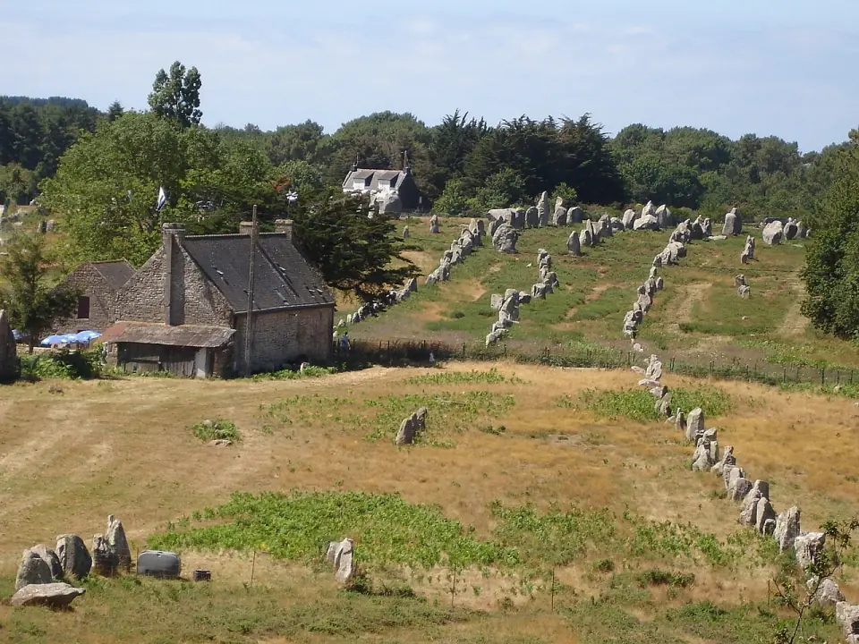 Alignement de Kermario : files de menhirs montant vers les arbres, avec une maison de pierre au premier plan