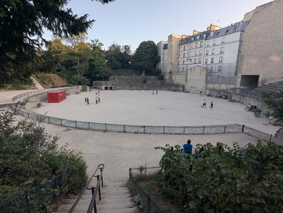 Vue des arènes de Lutèce : piste de sable, gradins et immeubles parisiens en arrière-plan