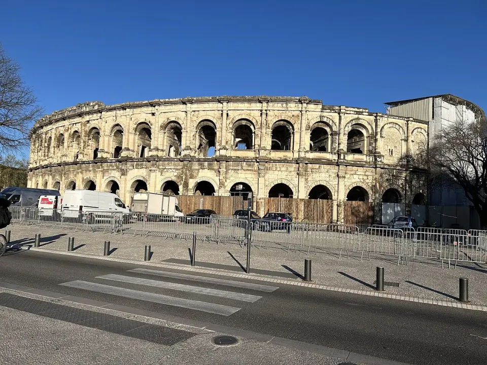 Les arènes de Nîmes depuis la rue, avec leurs arcades en pierre dorée sous un ciel bleu