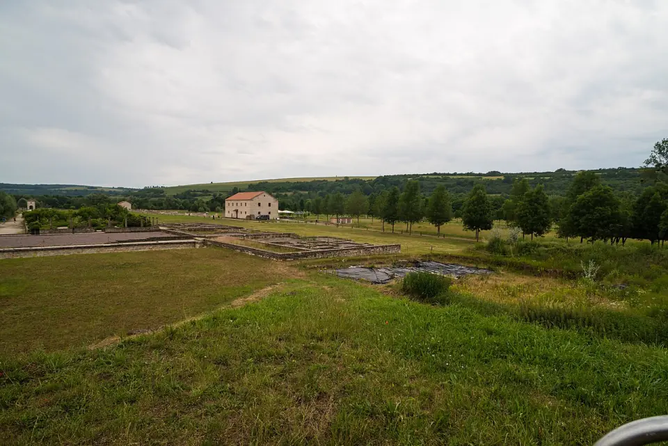 Murs bas de la ville romaine dans la vallée, avec un bâtiment de pierre à toit de tuiles au loin