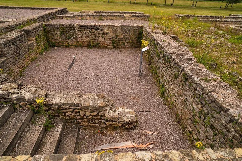Salle des thermes de Bliesbruck, murs de pierre, sol de gravier et marches de bois