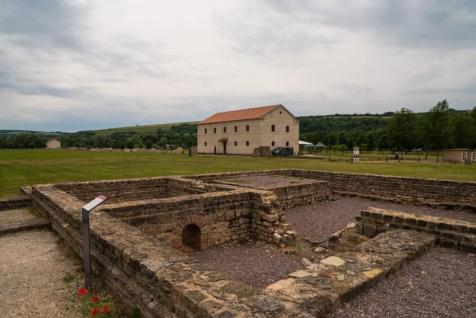 Murs de thermes gallo-romains avec une arche de brique et, derrière, un bâtiment à toit de tuiles