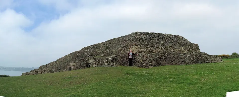Le cairn de Barnenez vu de l'est, avec un visiteur au pied du parement de pierres sèches