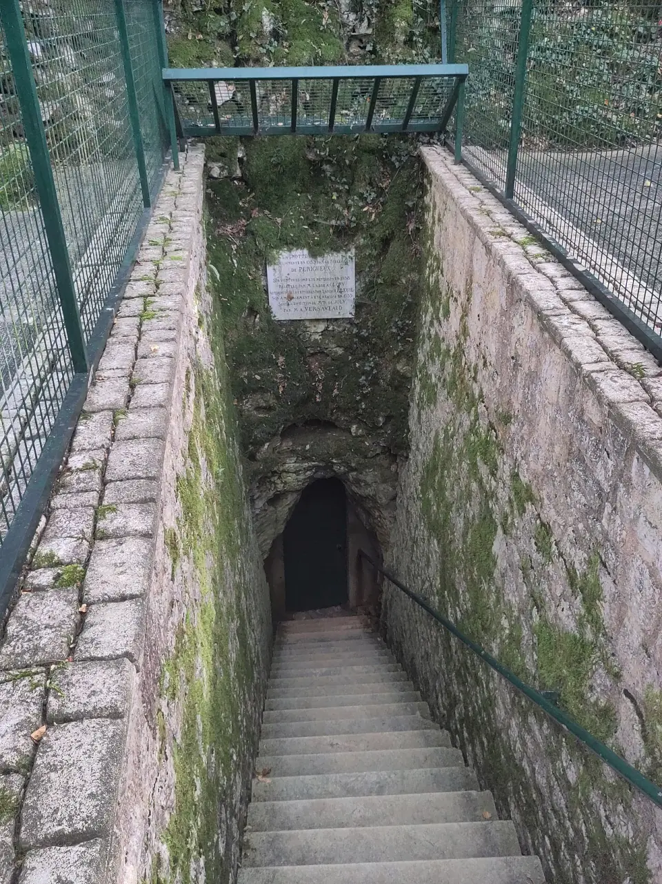 Porte d'entrée de la grotte de Villars, avec la plaque commémorative de la découverte et de l'ouverture