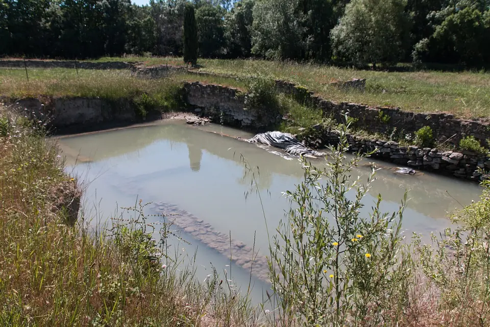 Fosse de fouille remplie d'eau, avec des murs de pierre sur les bords, à Lattara