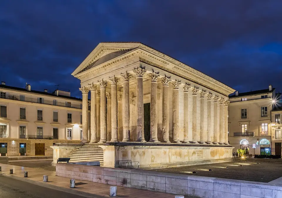 La Maison Carrée de Nîmes éclairée à la tombée de la nuit, avec son escalier et ses colonnes