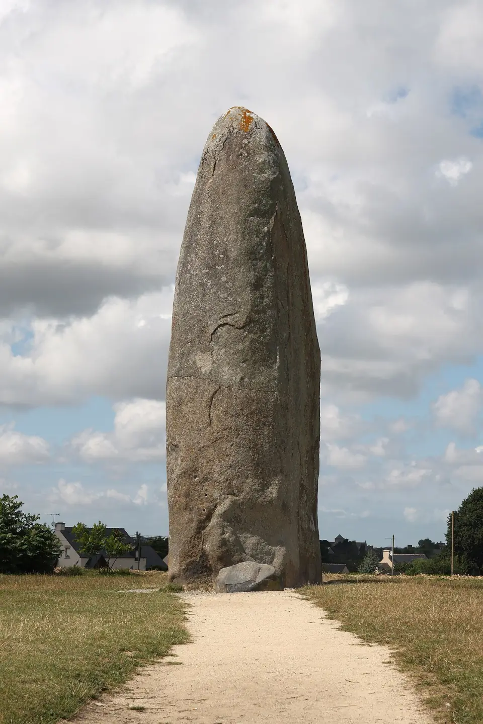 Le menhir de Champ-Dolent au bout d'un chemin sablé, sous un ciel nuageux