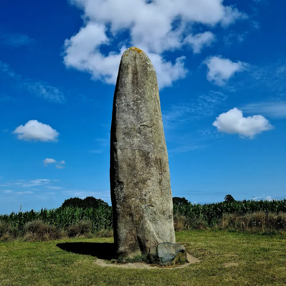 Le menhir de Champ-Dolent sous un ciel bleu, entouré de champs en plein été