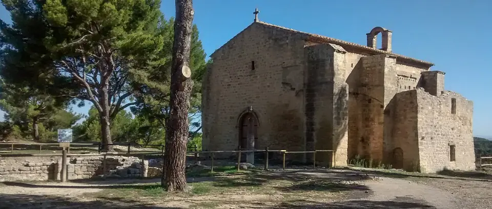 Façade de la chapelle Saint-Blaise, en pierre, au milieu des pins sous un ciel bleu