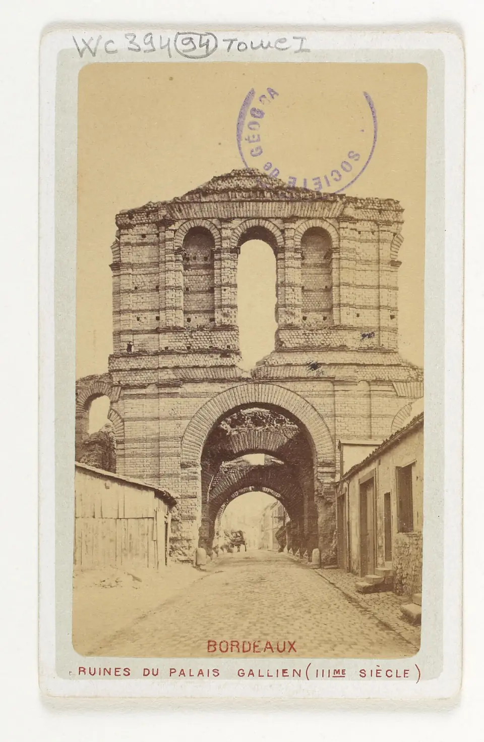 Ancienne photographie en sépia des ruines du palais Gallien, avec leur porte à arcades, rue étroite au premier plan