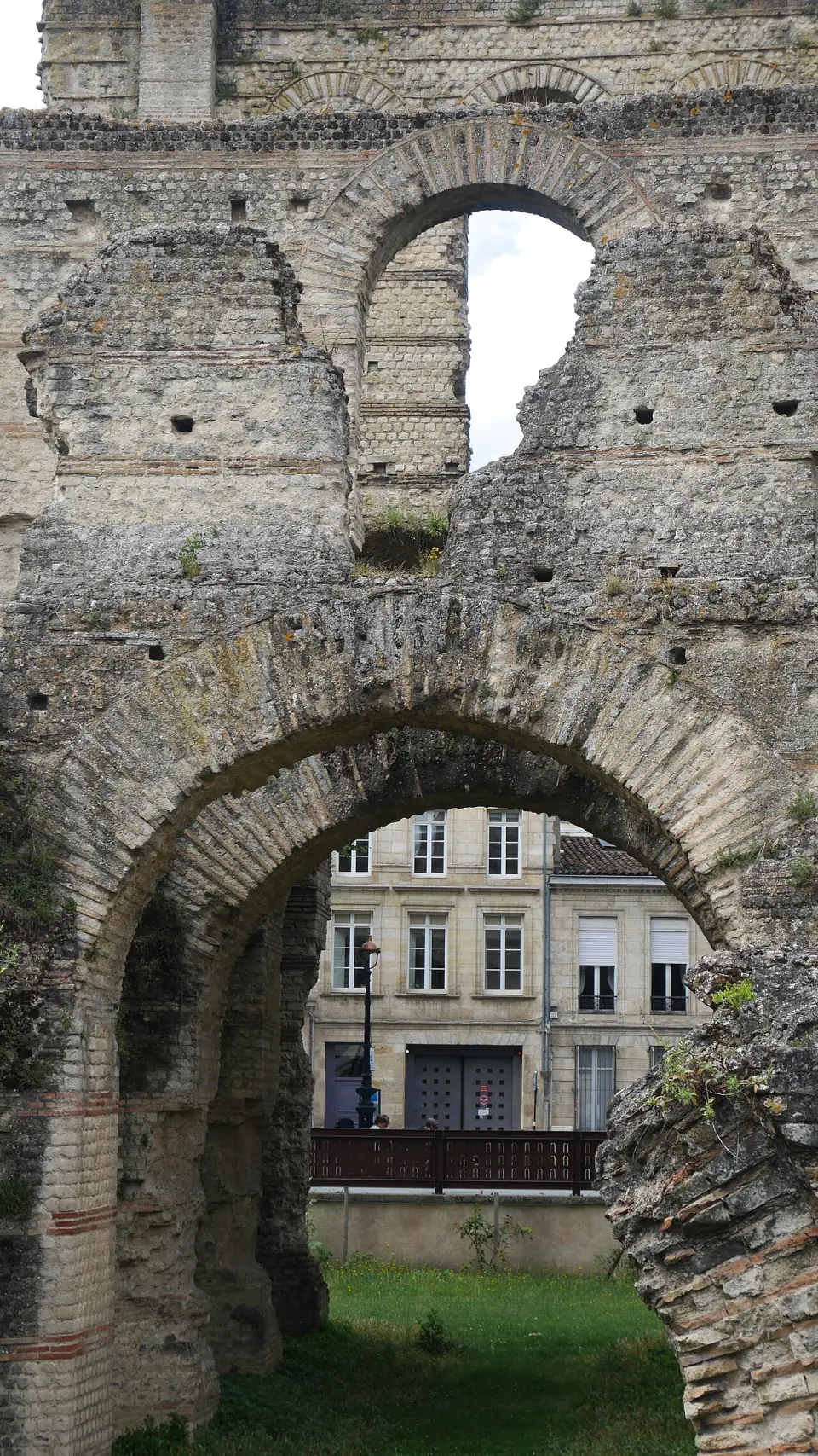Arcades de brique et de pierre du palais Gallien, avec la rue et des immeubles au fond
