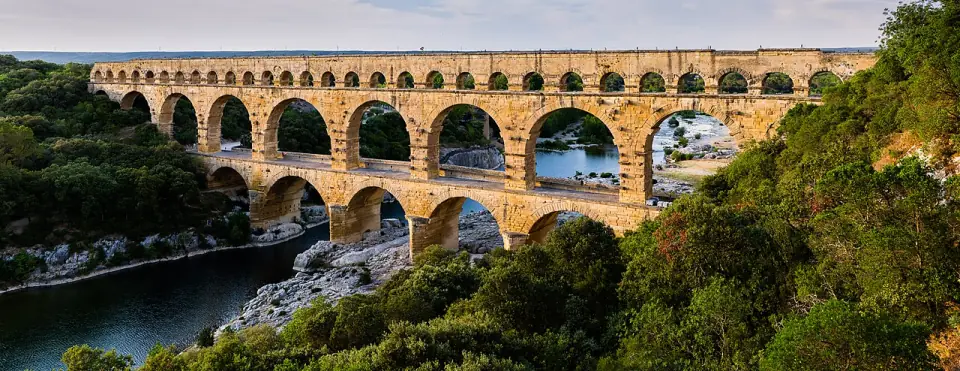 Le Pont du Gard en vue panoramique, ses arches dorées au-dessus de la rivière, entre rochers et végétation