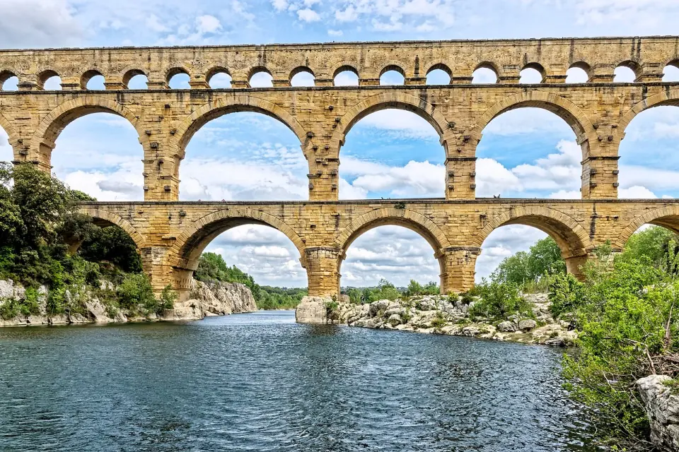 Les trois étages d'arches du Pont du Gard vus de face, au-dessus du Gardon, sous un ciel nuageux