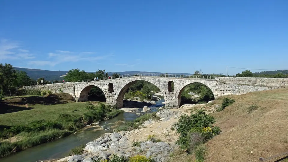 Le pont Julien vu de côté avec la rivière et des promeneurs sur le tablier