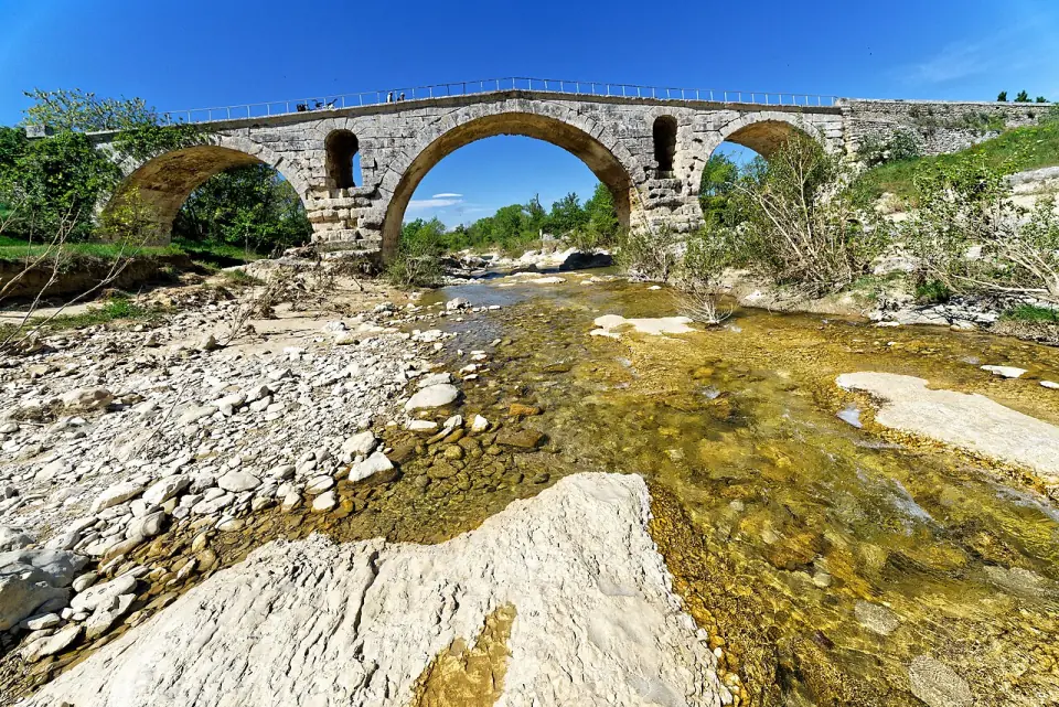 L'arche centrale du pont Julien, vue depuis le lit du Calavon sous un ciel bleu