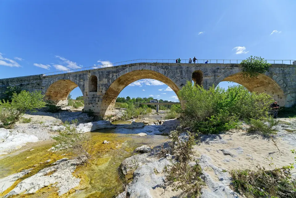 Le pont Julien traversé par des promeneurs, avec la rivière au premier plan