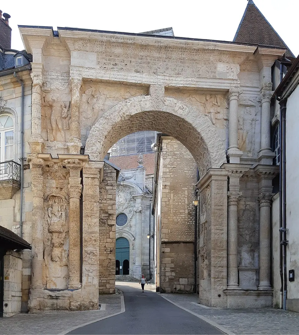 La porte Noire de Besançon, arc de triomphe romain en pierre claire, avec une façade d'église au fond
