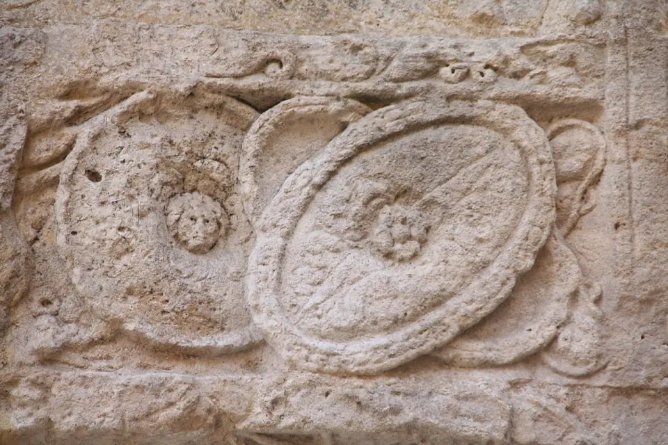 Détail de la porte Noire : deux disques sculptés ornés de petits visages, dans un cadre de pierre