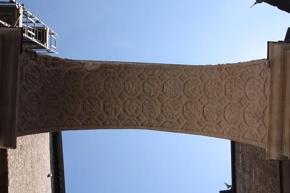 Vue de dessous de l'arc de la porte Noire : voûte décorée de caissons octogonaux sculptés, sous un ciel bleu
