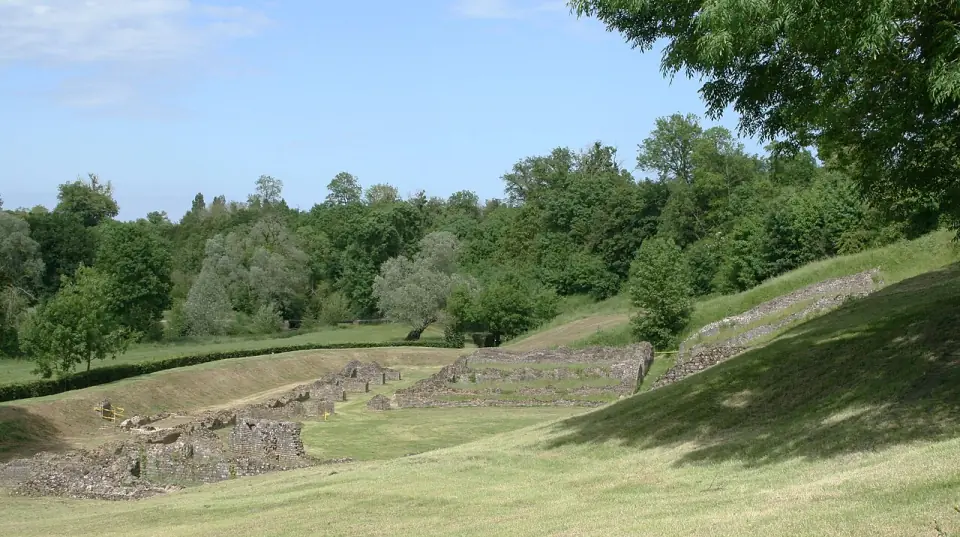 Ruines du théâtre romain de Sanxay : gradins et murs de pierre sur l'herbe, au milieu des arbres