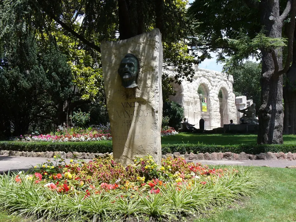 Monument à Vincent van Gogh dans un jardin fleuri, avec les arcades du théâtre antique d'Arles au fond