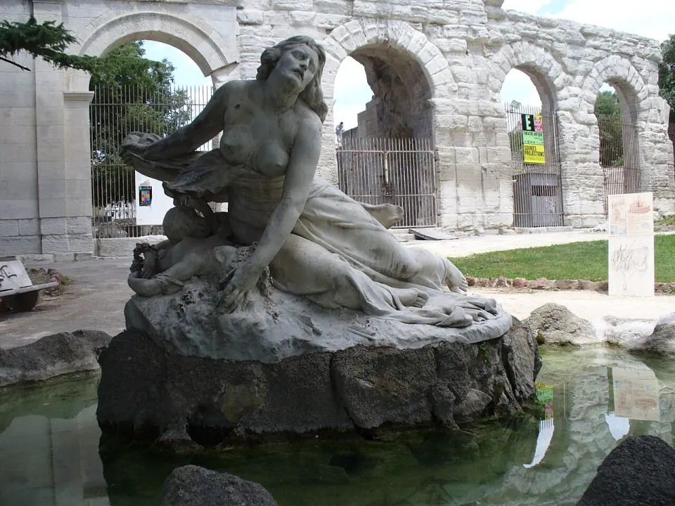 Fontaine ornée d'une sculpture de femme couchée, devant les arcades du théâtre antique d'Arles