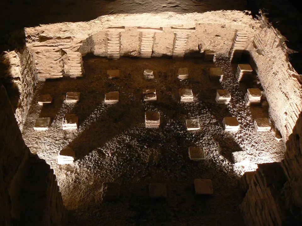 Hypocauste des thermes d'Entrammes : colonnettes de briques alignées sur le sol, éclairées dans la pénombre