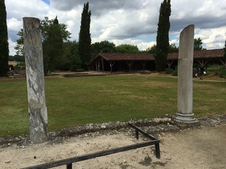 Deux colonnes dressées dans la cour-jardin de la villa de Séviac, avec la toiture des vestiges au fond