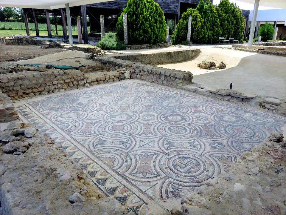 Mosaïque polychrome de la villa de Séviac, abritée sous une toiture, avec des cyprès et des colonnes en fond